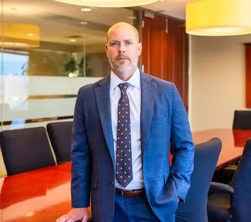 Portrait of a serious man in a blue suit with a patterned tie, standing in a corporate office setting with a conference ta...
